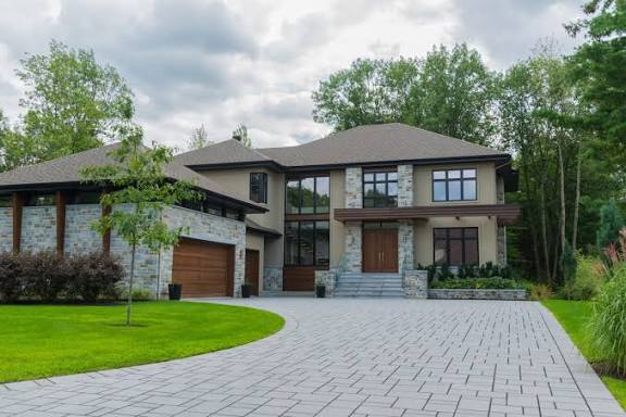 Two-storey stone home with a broad driveway and mature trees
